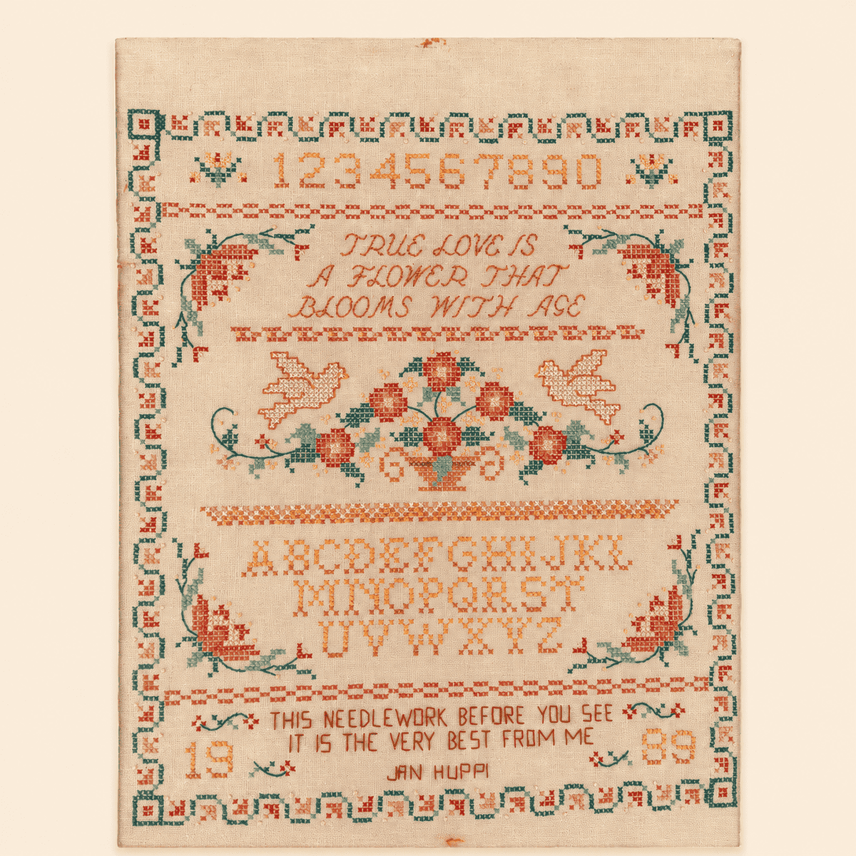 Full view of hand-stitched sampler with alphabet and floral border