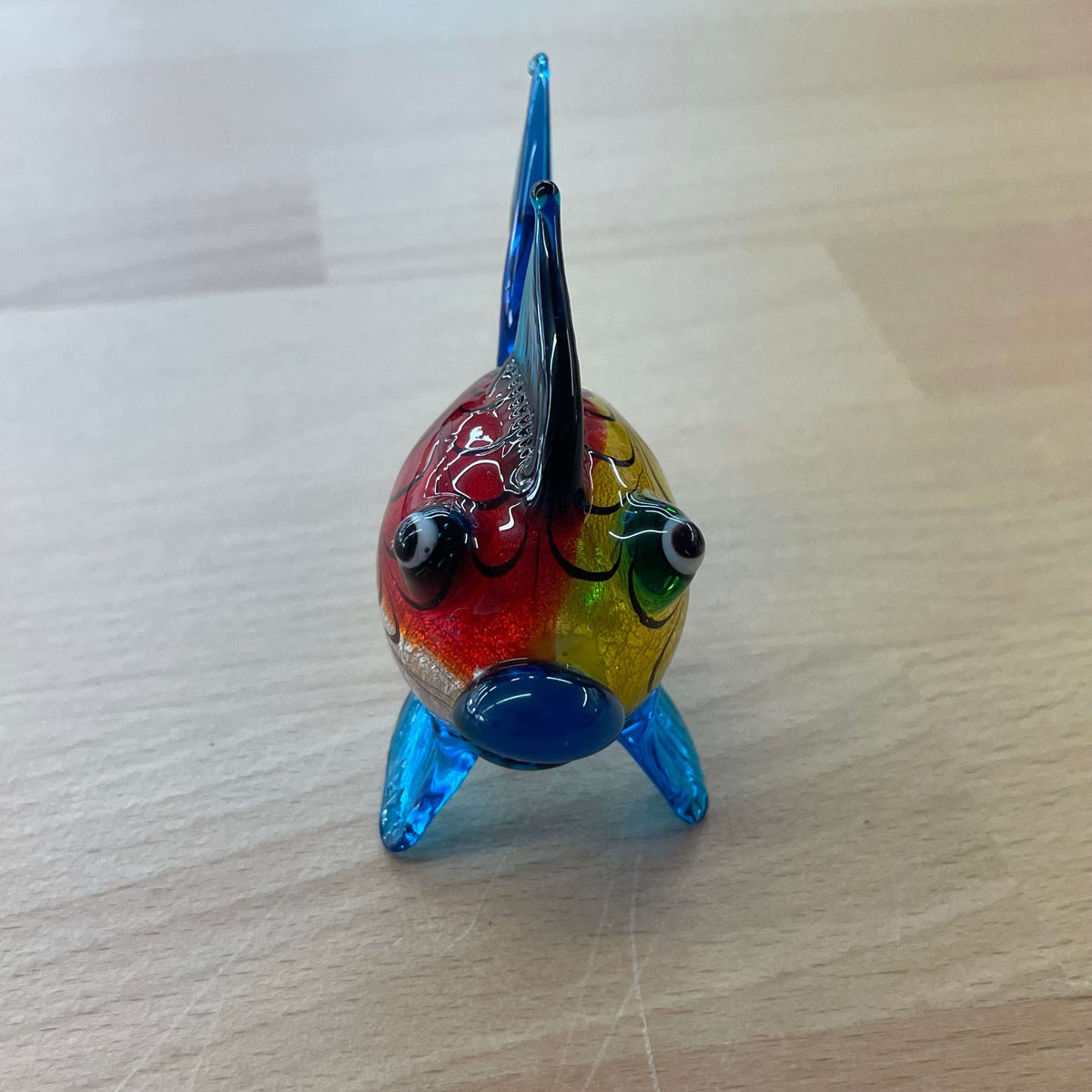 Art glass rainbow fish — head-on view on its blue glass fins