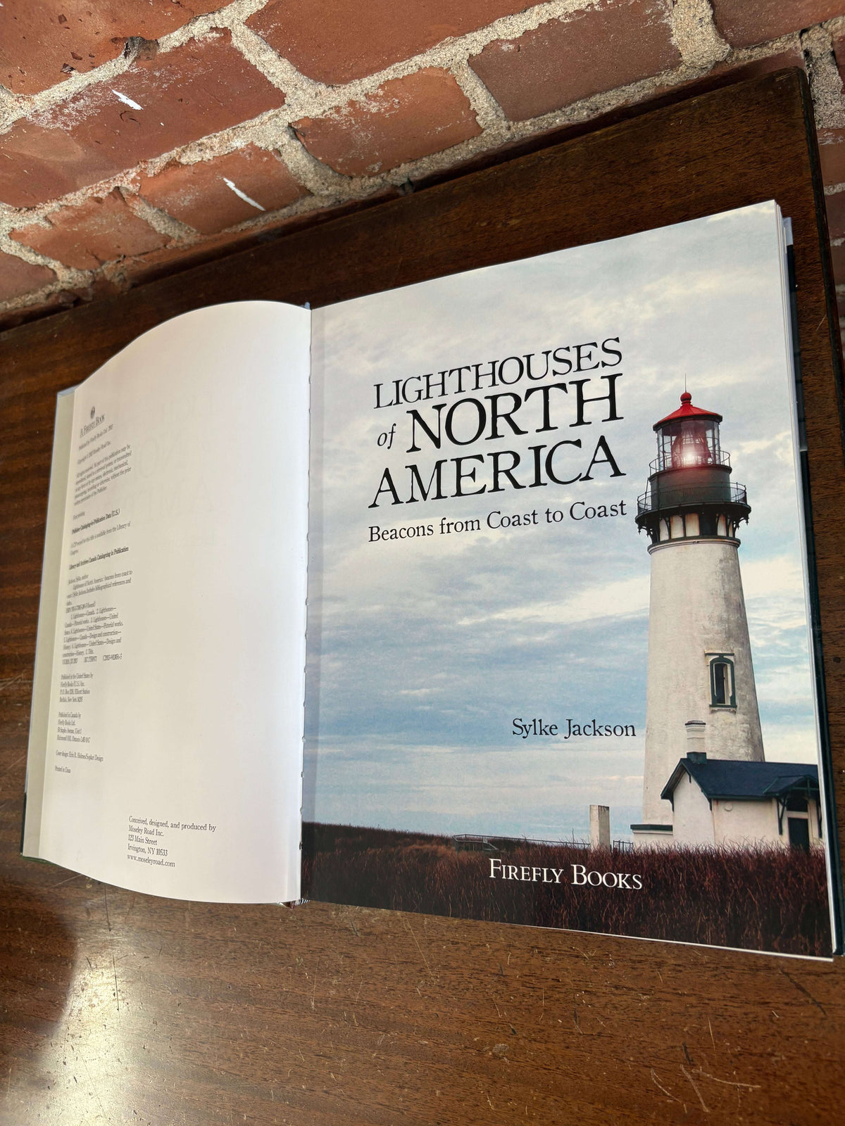 Lighthouses of North America by Sylke Jackson, open to a page showing a white coastal lighthouse