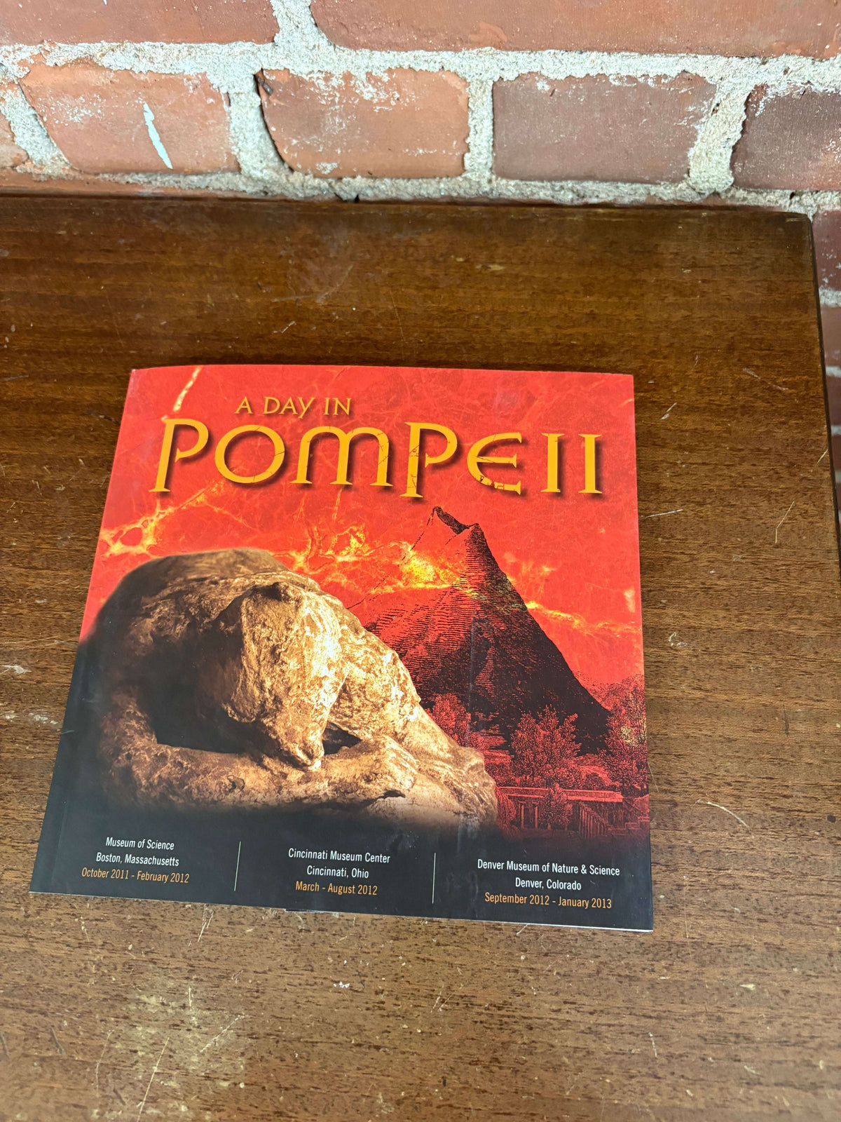 Cover of A Day in Pompeii exhibition catalog, showing a plaster body cast with Vesuvius erupting behind it