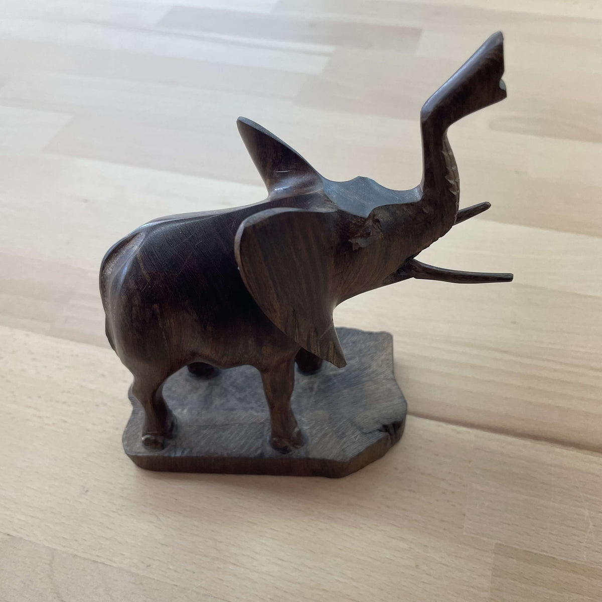 Hand-carved dark hardwood elephant figurine with trunk raised, on a natural wood base