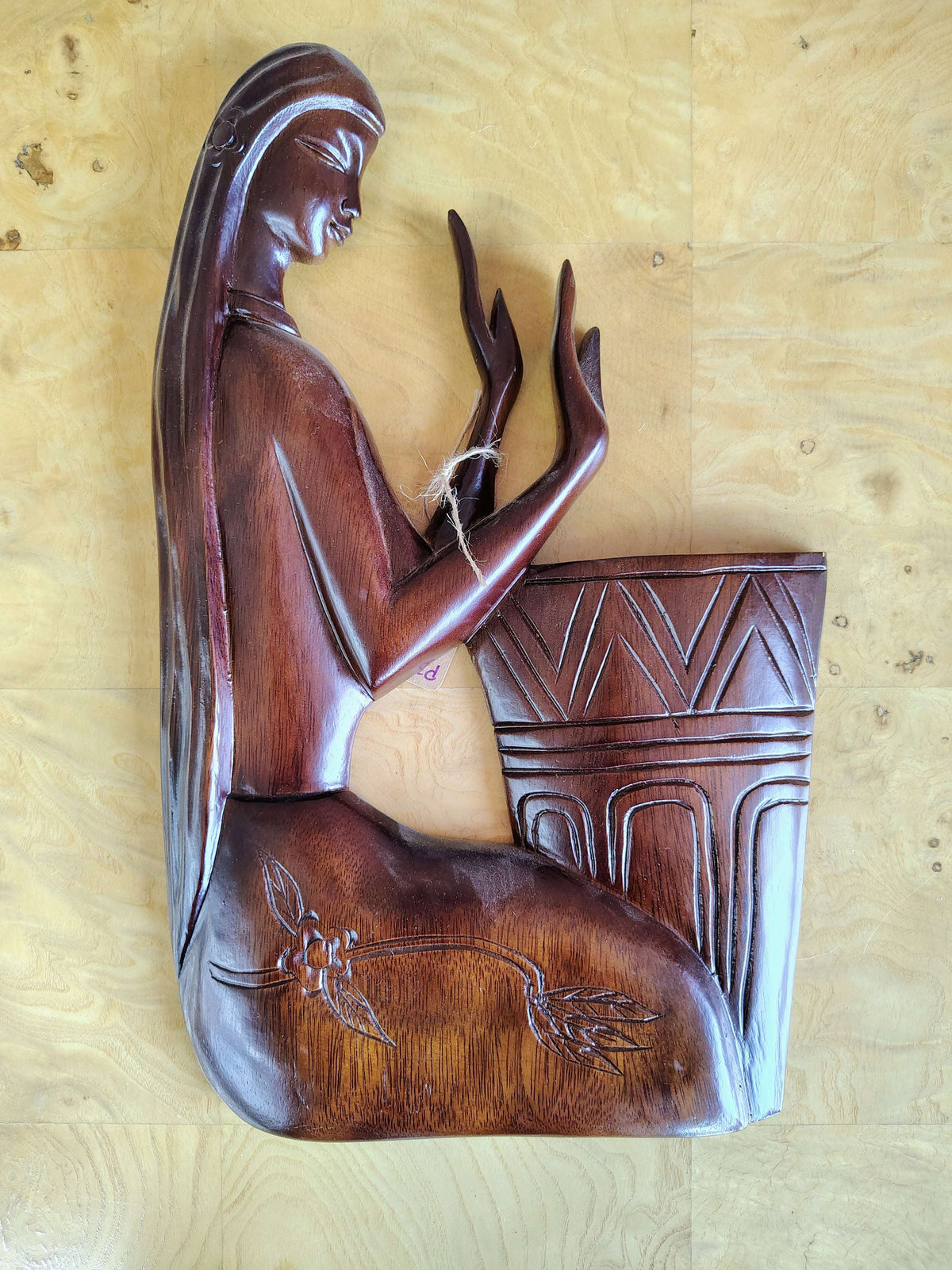 Carved wood wall panel of a kneeling woman in deep relief beside a carved vessel