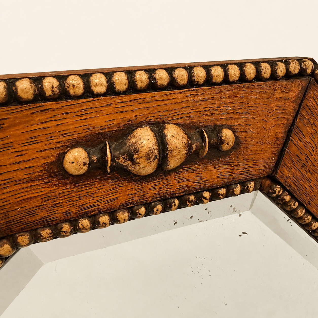 Close detail of a turned urn finial and beaded border on the oak mirror frame