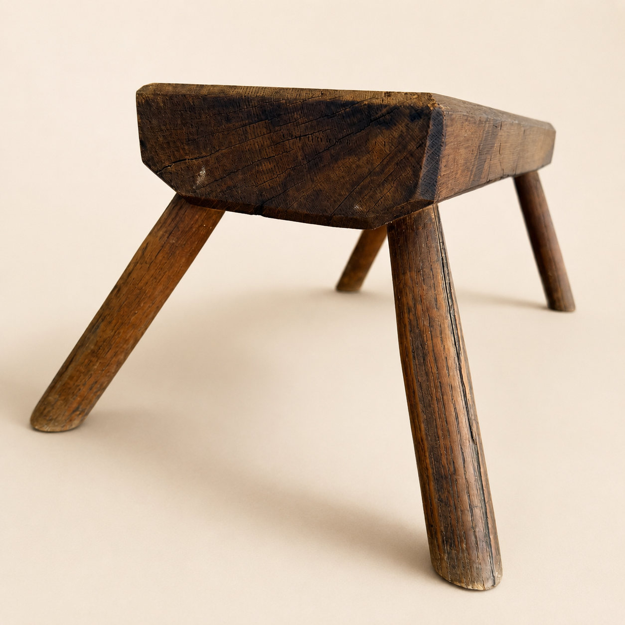 End profile of antique hand-hewn plank stool standing on splayed legs