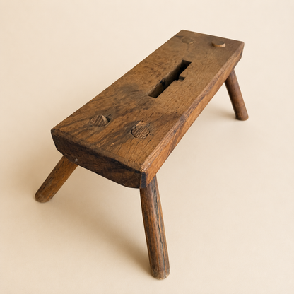 Angled view of antique primitive plank foot stool with pegged legs and handhold slot
