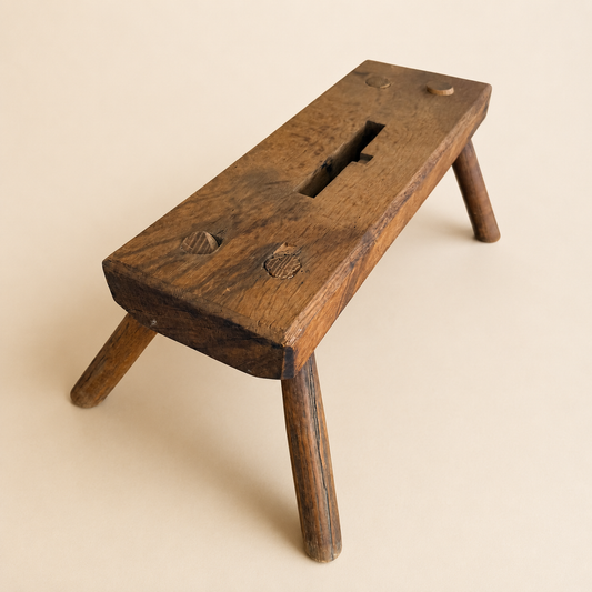 Angled view of antique primitive plank foot stool with pegged legs and handhold slot