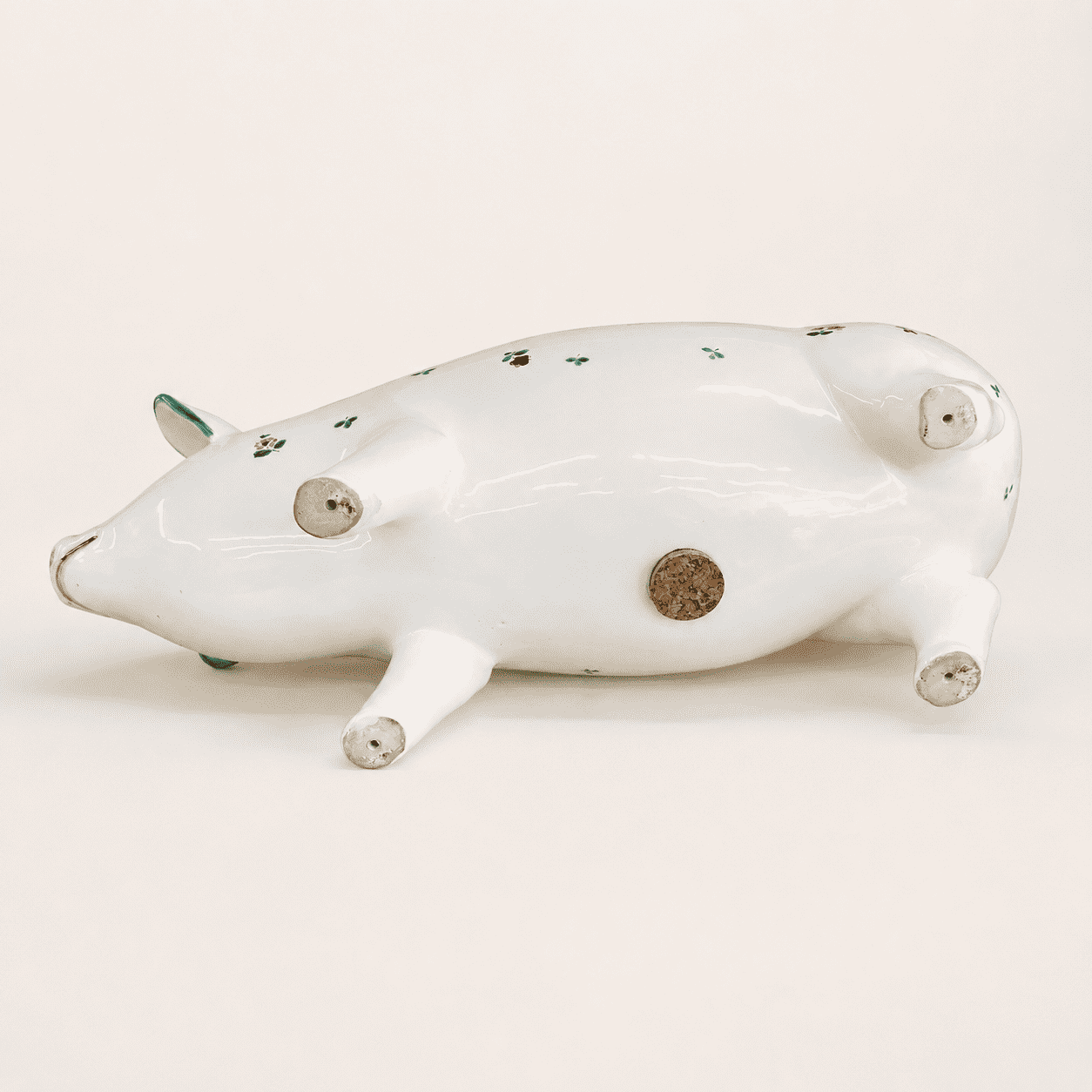 Large hand-painted pig bank on its side showing cork belly stopper and unglazed feet