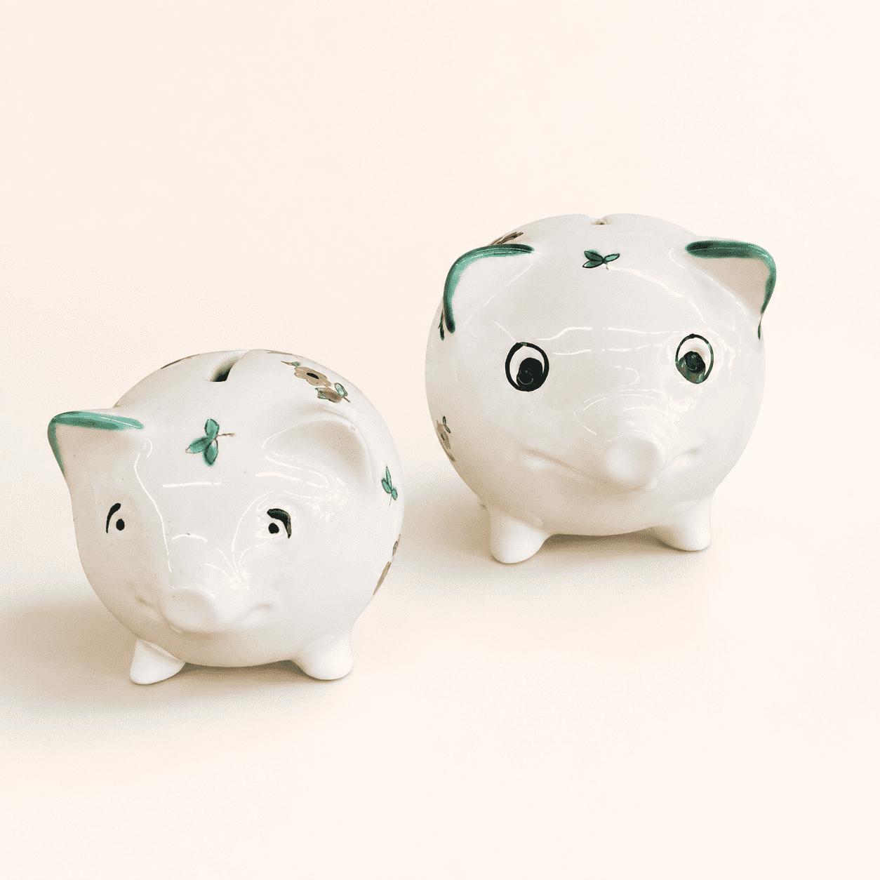 Two small hand-painted piggy banks showing faces and scattered-flower pattern