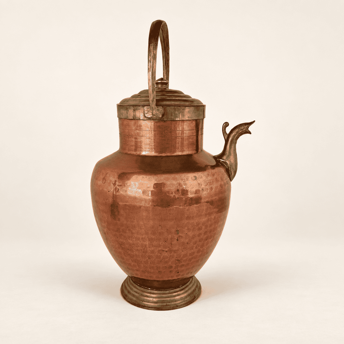 Hammered copper ewer at an angle showing the brass lid, handle, and bird spout