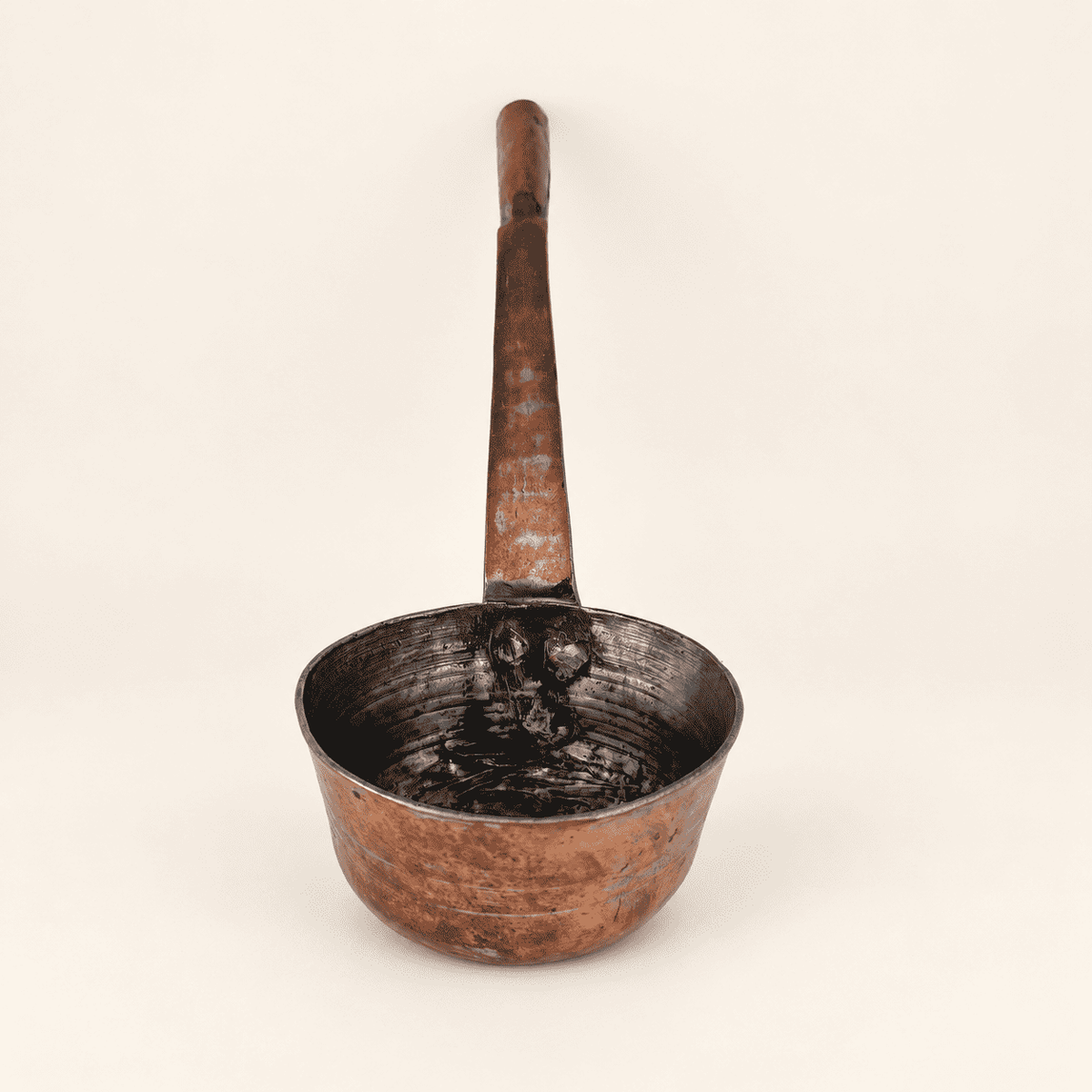 The copper dipper upright, deep bowl below the long forged handle
