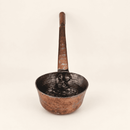 The copper dipper upright, deep bowl below the long forged handle