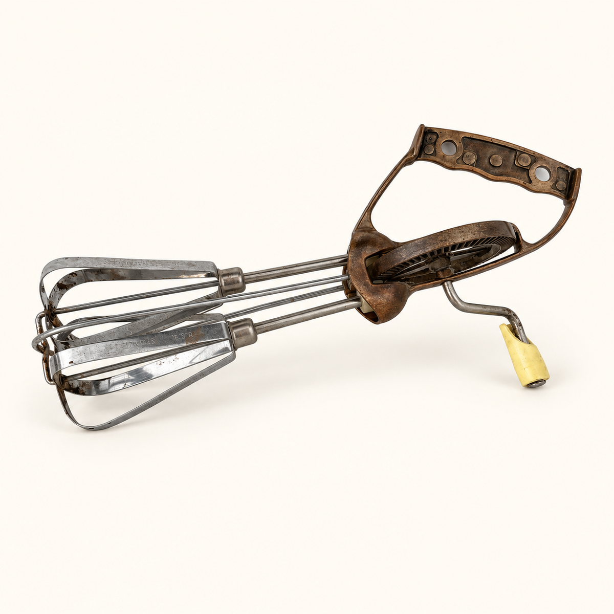 Vintage rotary egg beater lying down, copper D-grip handle and cream knob crank, stainless beaters