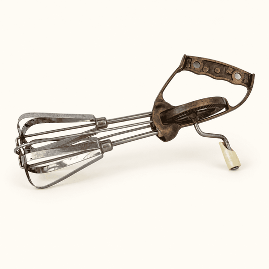 Vintage rotary egg beater lying down, copper D-grip handle and cream knob crank, stainless beaters