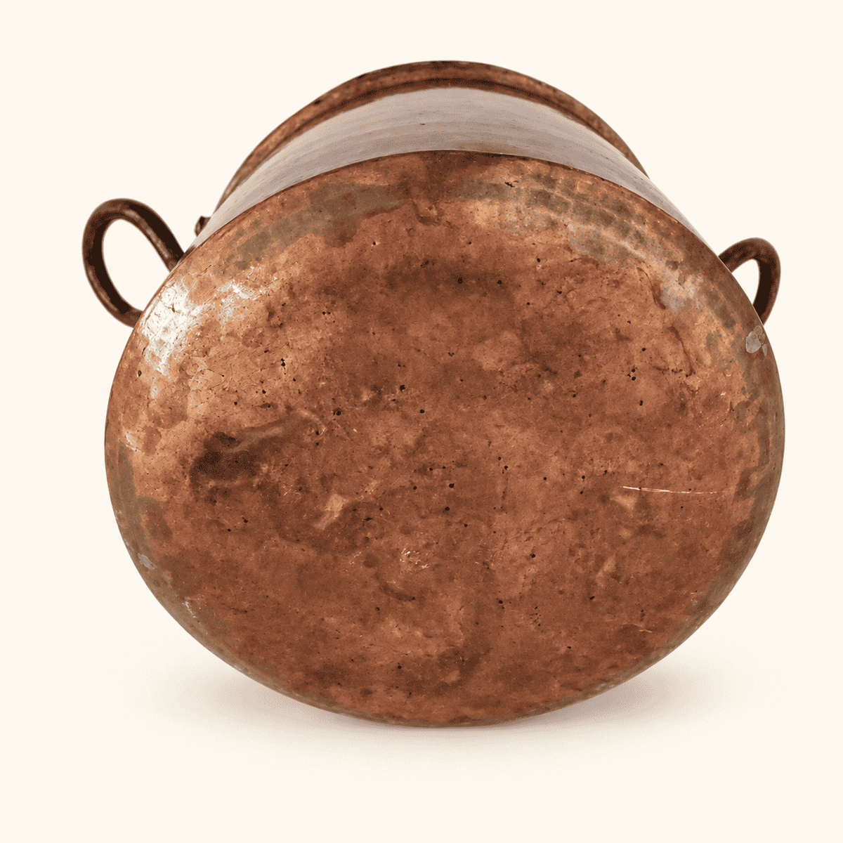 Rounded hand-forged base of the copper pot with hammer marks, both loop handles visible