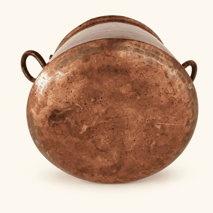 Rounded hand-forged base of the copper pot with hammer marks, both loop handles visible
