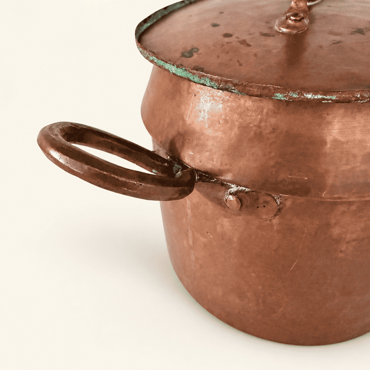 Close detail of a riveted loop handle and the green verdigris along the lid rim