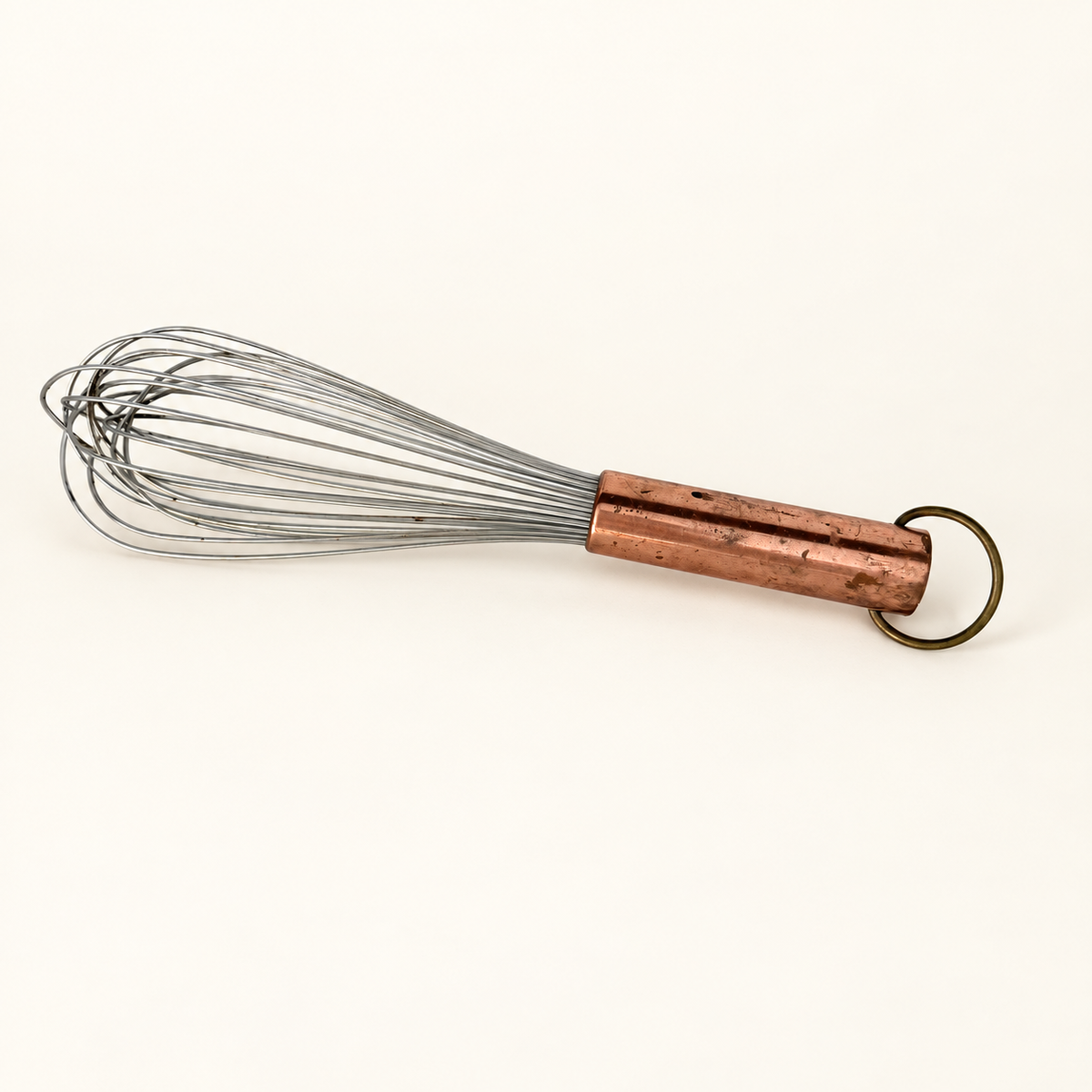 The whisk laid out, wire head to the left and copper handle with brass ring to the right