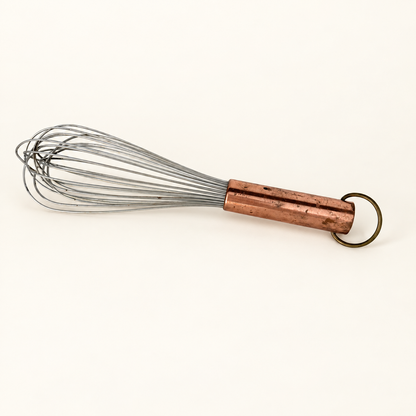 The whisk laid out, wire head to the left and copper handle with brass ring to the right