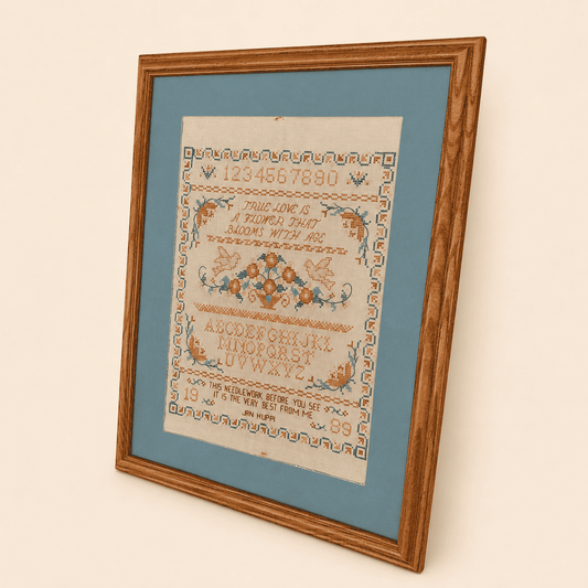 Angled view of 1989 cross stitch sampler in oak frame with blue mat