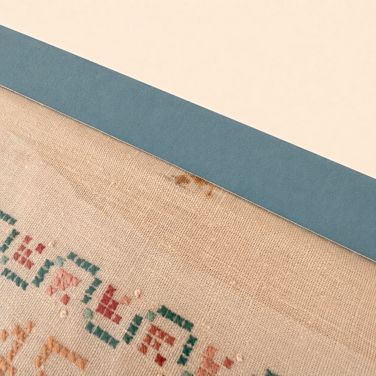 Detail of small brown stain on sampler linen