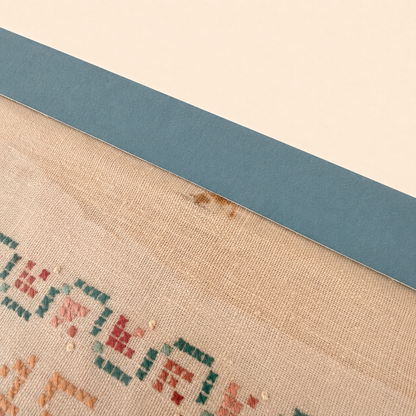 Detail of small brown stain on sampler linen
