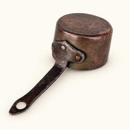 Rounded hand-forged base of the copper saucepan and the riveted iron handle flange