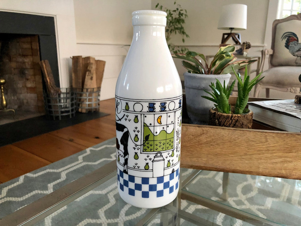 Back of the milk glass bottle showing a shelf of blue teacups and a window with green hills and a crescent moon