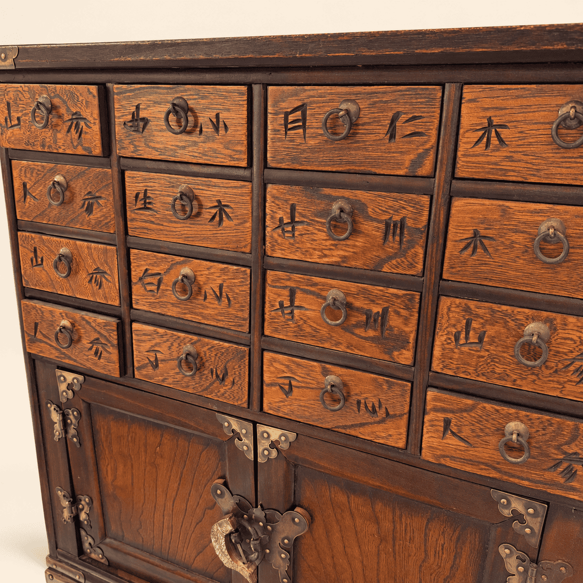 Close view of figured elm drawer fronts with carved characters and brass ring pulls