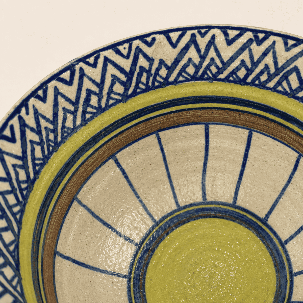 Detail of hand-painted blue zigzag and yellow sunburst glaze inside studio pottery bowl