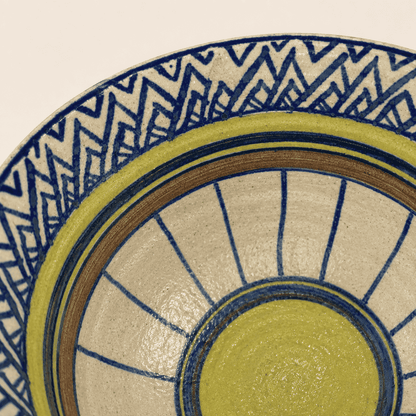 Detail of hand-painted blue zigzag and yellow sunburst glaze inside studio pottery bowl