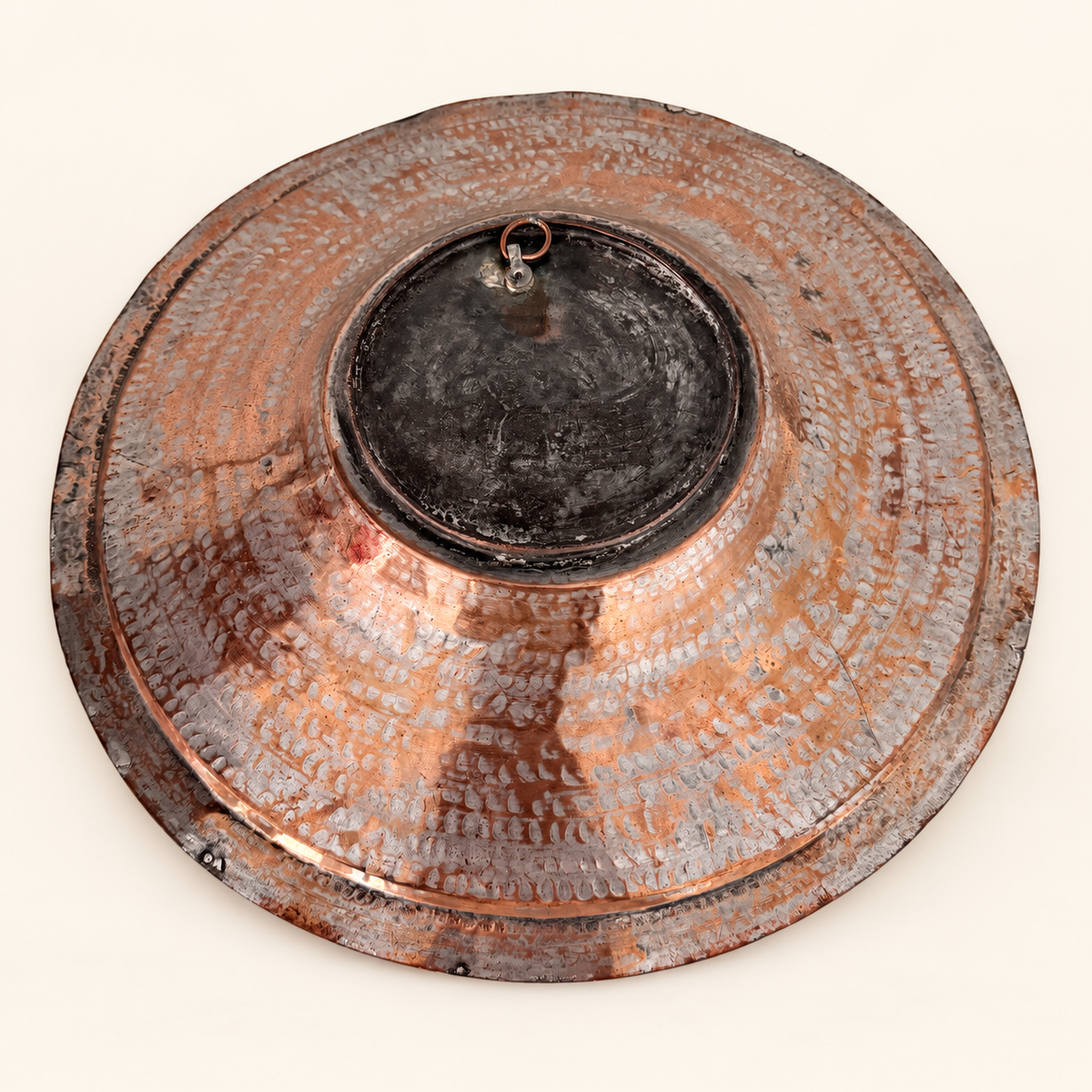 Back of the copper charger at an angle showing the raised domed center and copper hanging ring