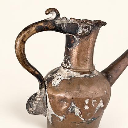 Arched handle with a scrolled thumb rest and the tin-washed neck of the copper ewer