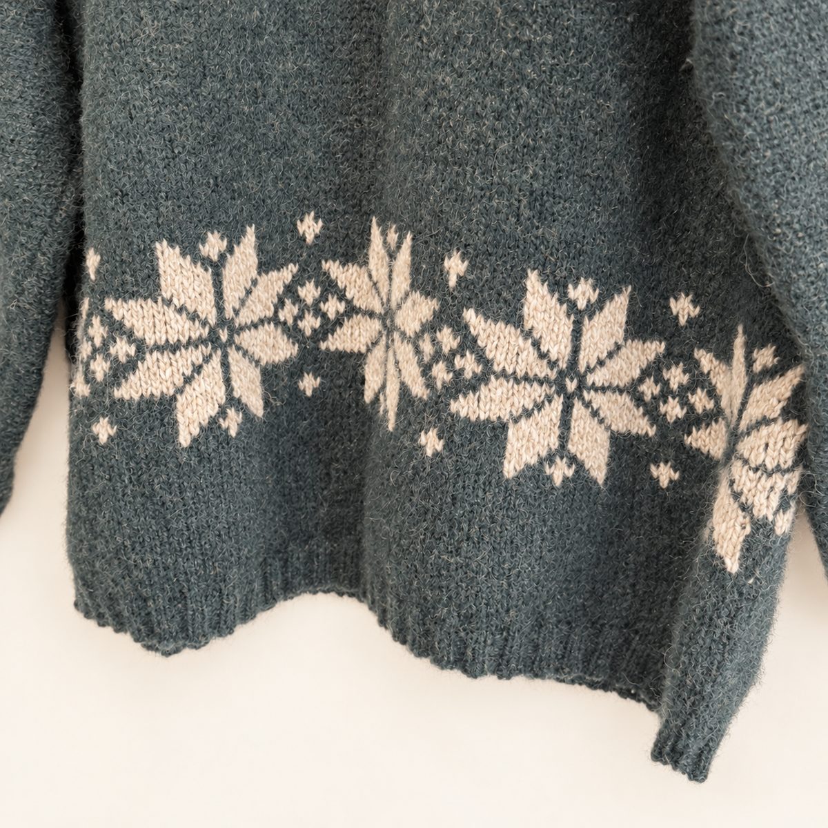 Snowflake band across the hem of a green wool sweater, close-up