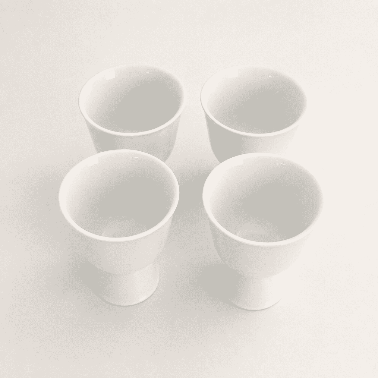Angled top view of four minimalist white porcelain footed cups