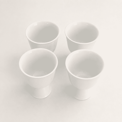 Angled top view of four minimalist white porcelain footed cups
