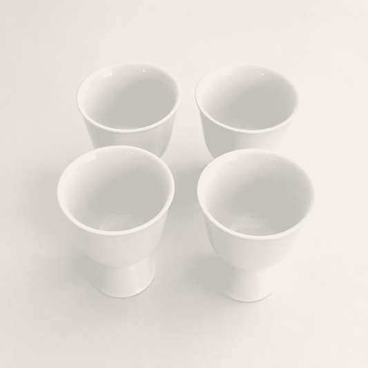 Angled top view of four minimalist white porcelain footed cups
