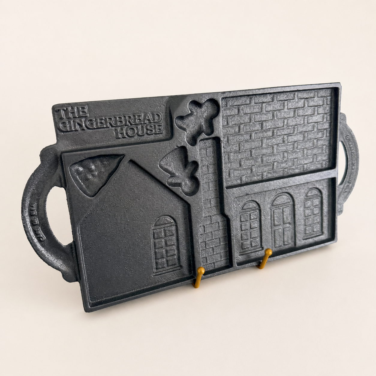 Cast iron gingerbread house mold displayed upright on a stand