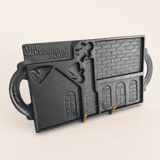 Cast iron gingerbread house mold displayed upright on a stand